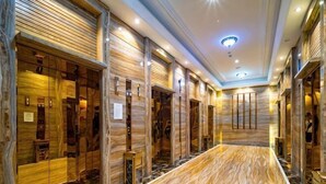 Ένας διάδρομος ξενοδοχείου με ξύλινη επένδυση στους τοίχους, μαρμάρινο δάπεδο και έναν κεντρικό χώρο.