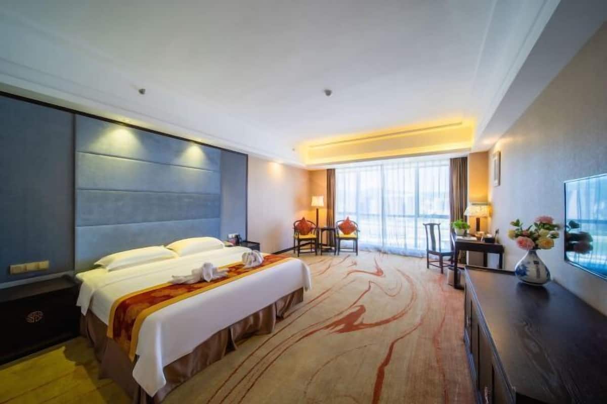 Ein Hotelzimmer mit einem großen Bett, einem Schreibtisch, einem Sessel und einem Fenster mit Vorhängen.