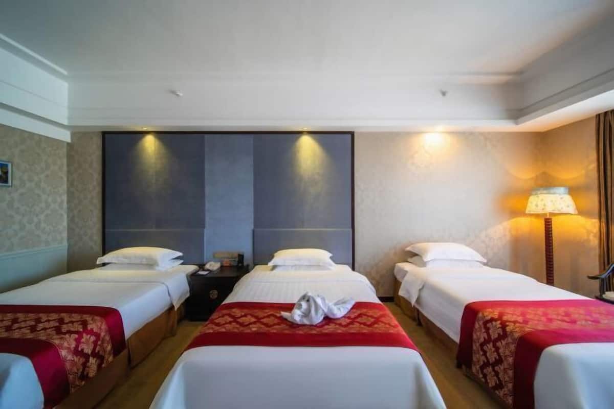 Ein Hotelzimmer mit zwei Betten, einem Nachttisch, einer Lampe und einem an der Wand montierten Fernseher.
