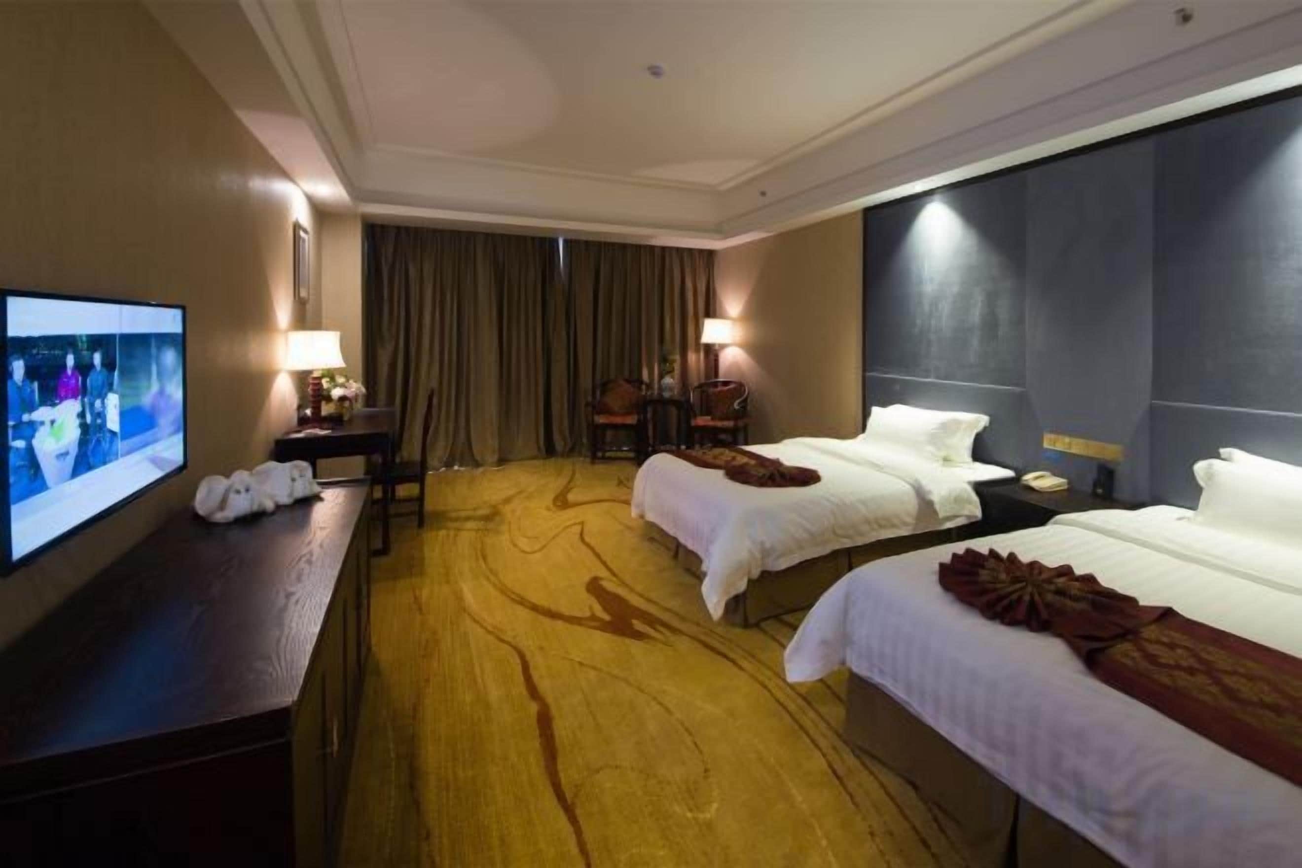 Habitación de hotel con dos camas, televisión, escritorio y un amplio ventanal.