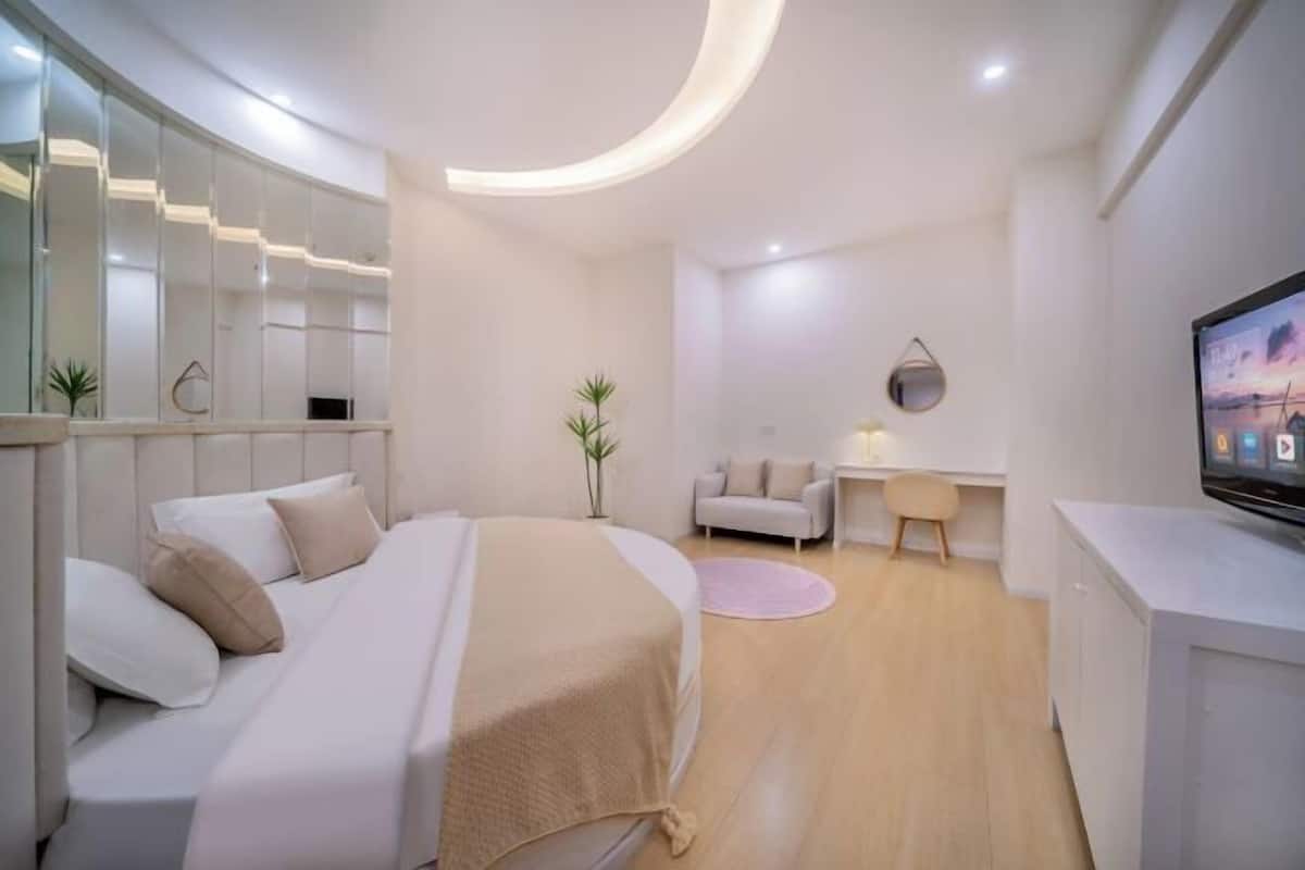 A modern bedroom with a bed, bedside table, TV, and a desk with a chair.