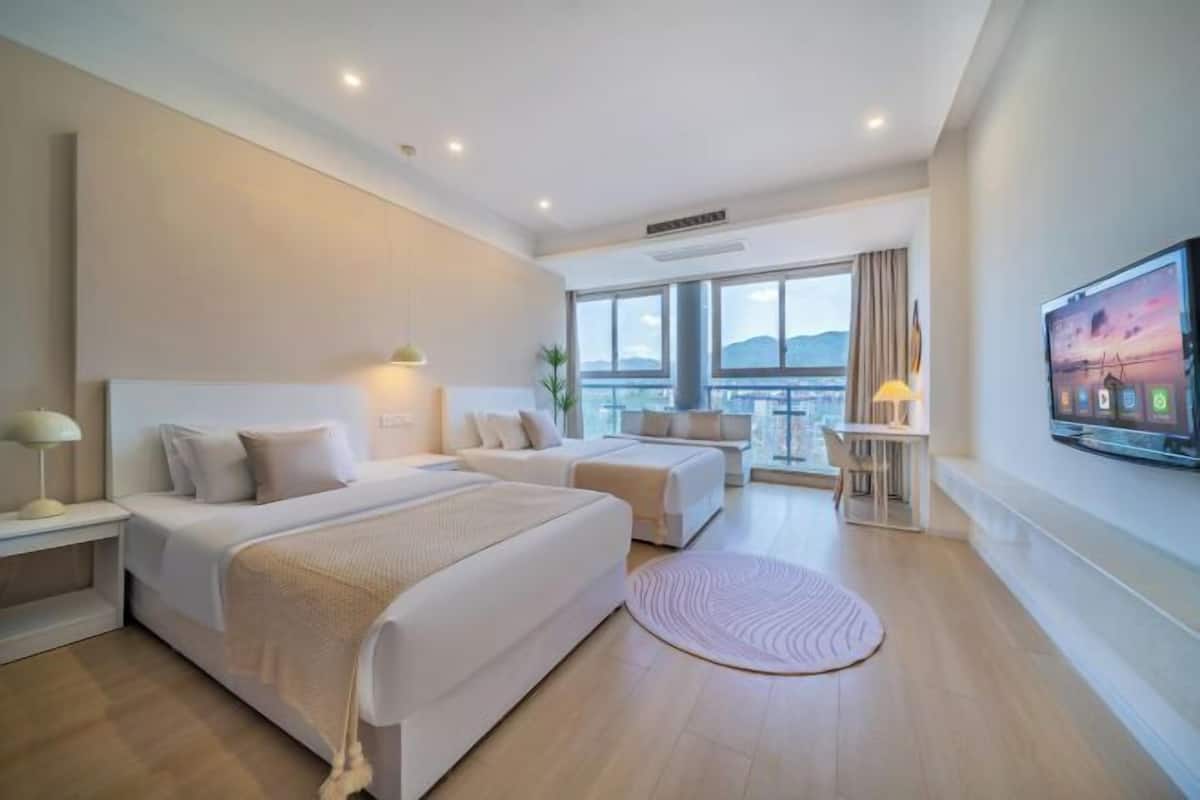 A hotel room with two beds, a sofa, a TV, and a balcony with a view.