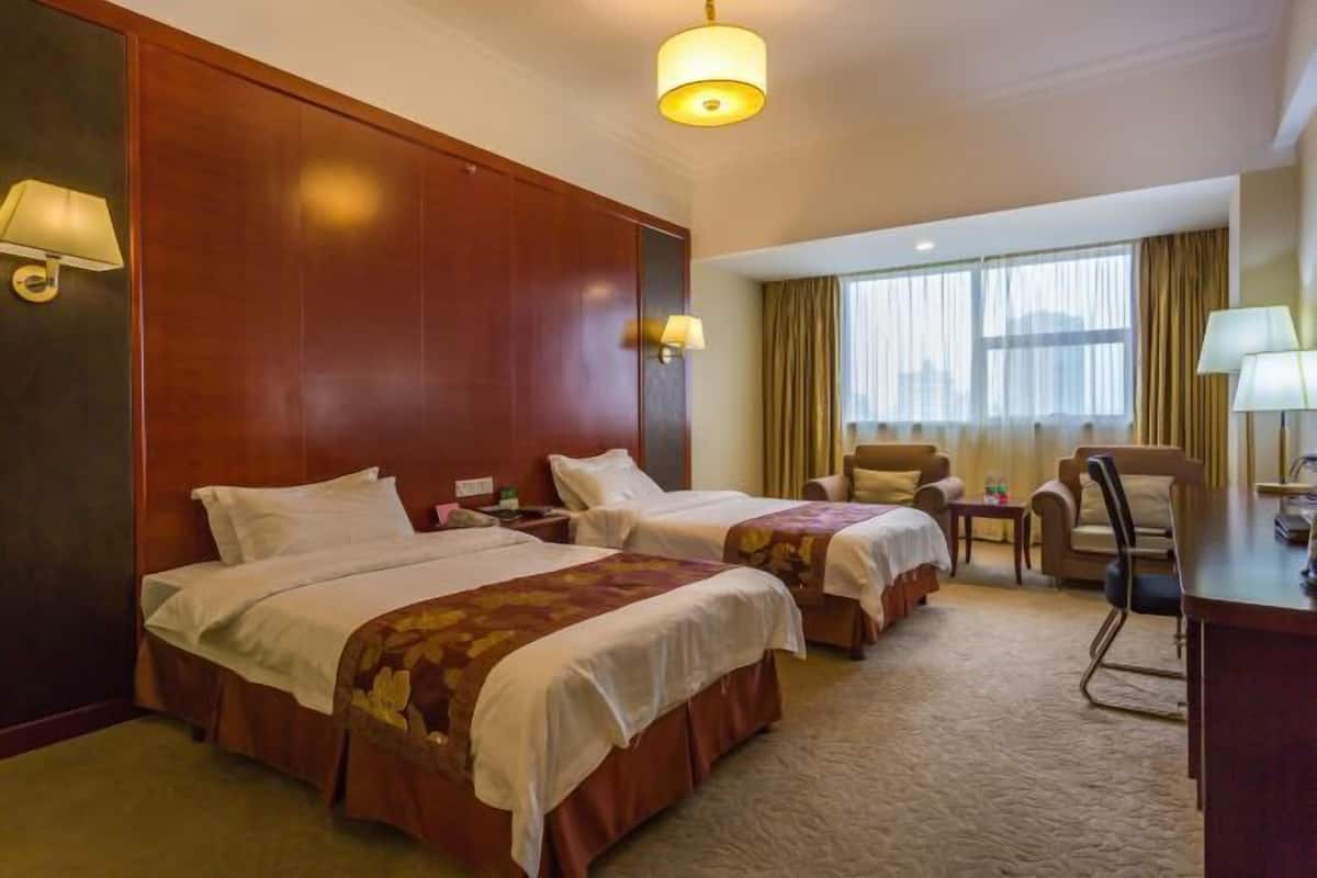 A hotel room with two beds, a desk, a chair, and a window with curtains.