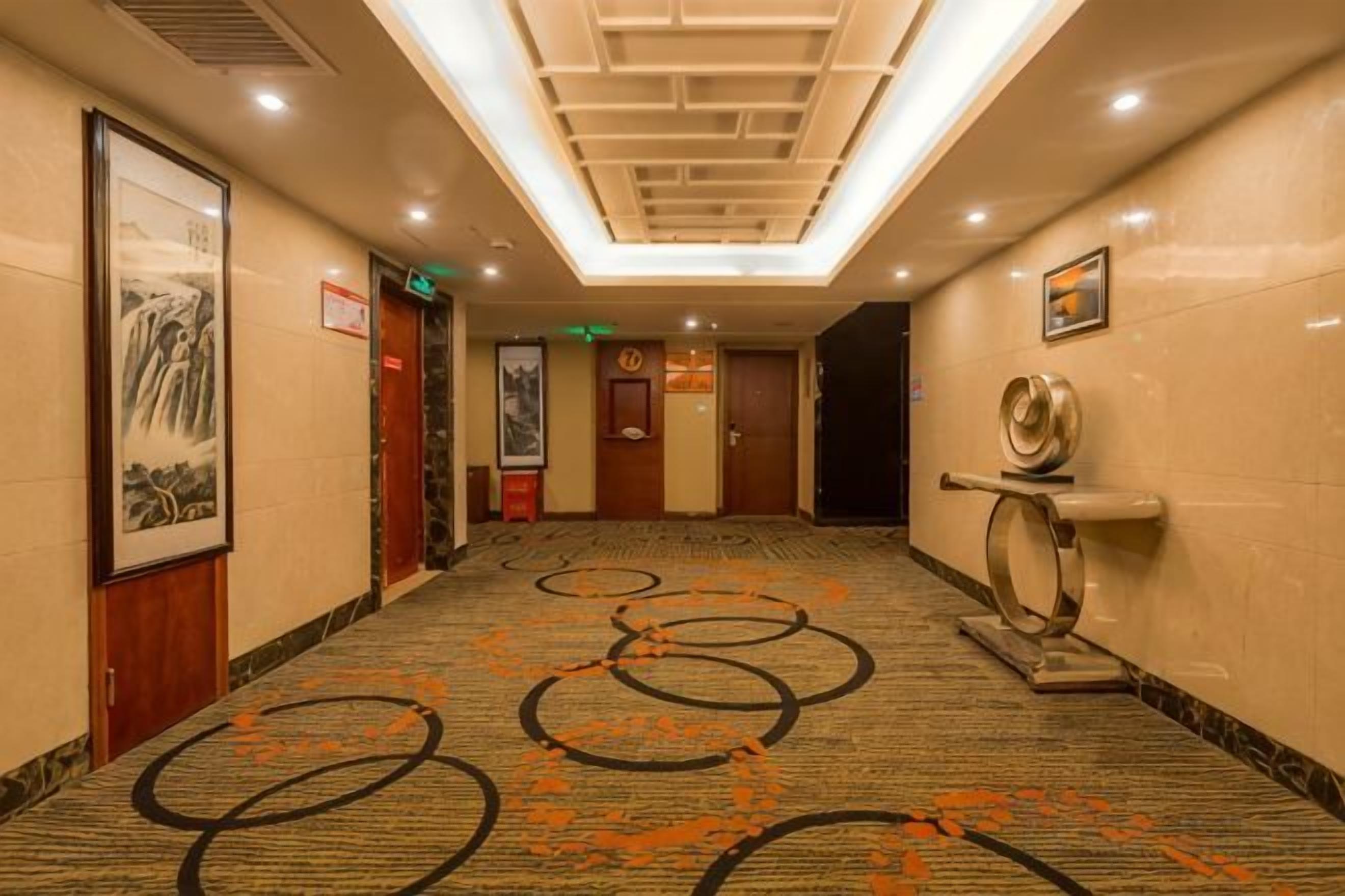 Un pasillo de hotel con alfombra estampada, obras de arte enmarcadas en las paredes y un diseño de techo moderno.