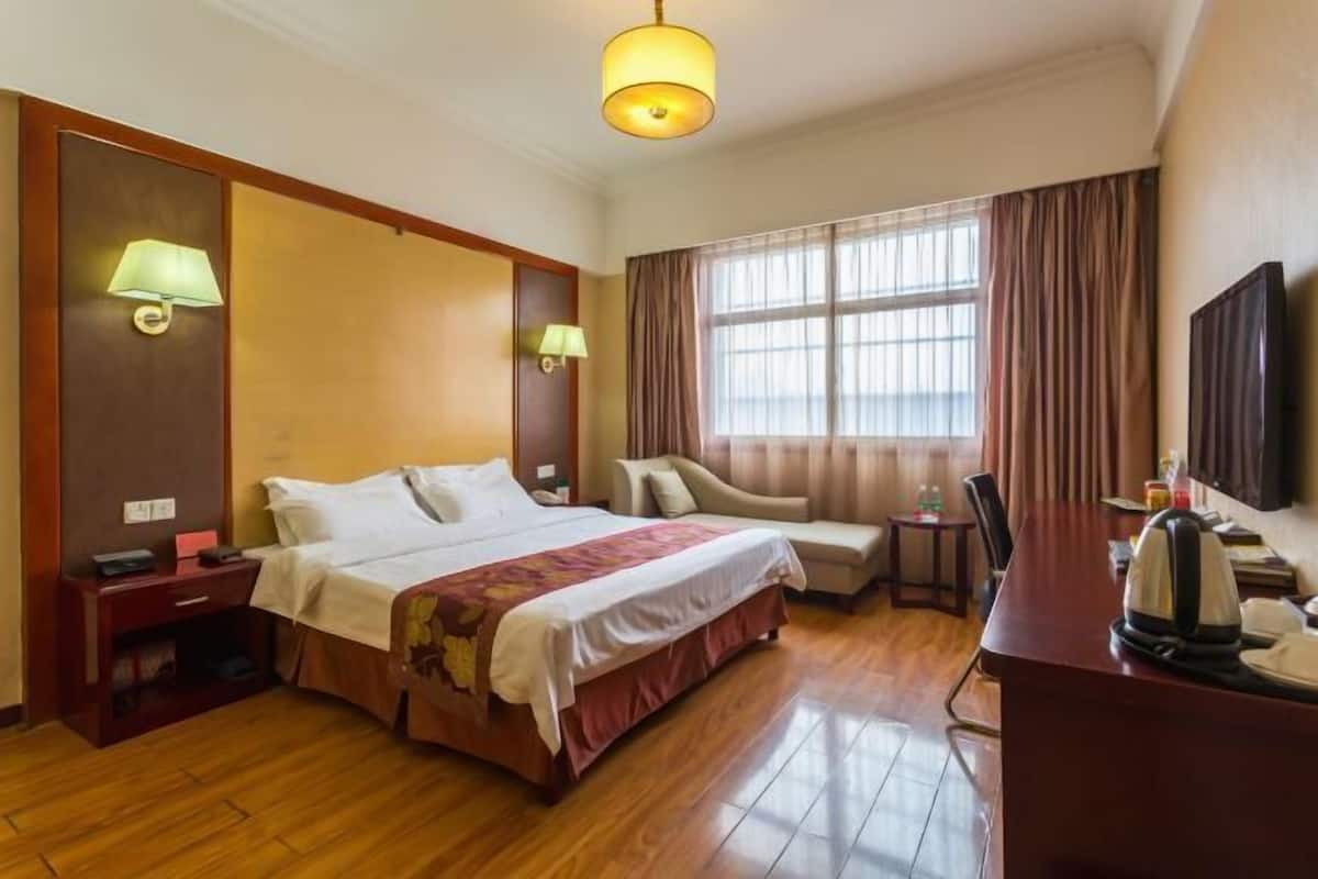 A hotel room with a bed, bedside lamps, a desk, a chair, a television, and a window with curtains.