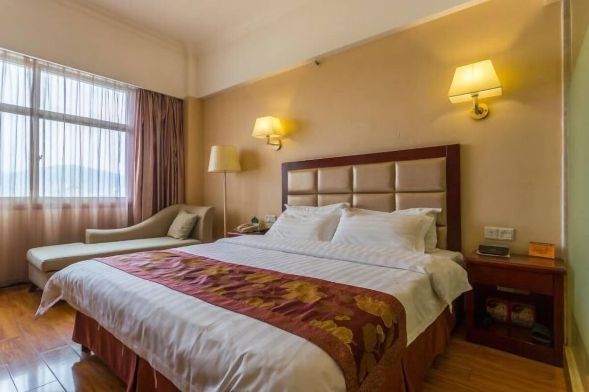 A hotel room with a large bed, two bedside tables, a chair, and a window with curtains.