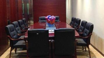 A conference room with a rectangular table surrounded by chairs, a floral centerpiece, and a red carpeted floor.