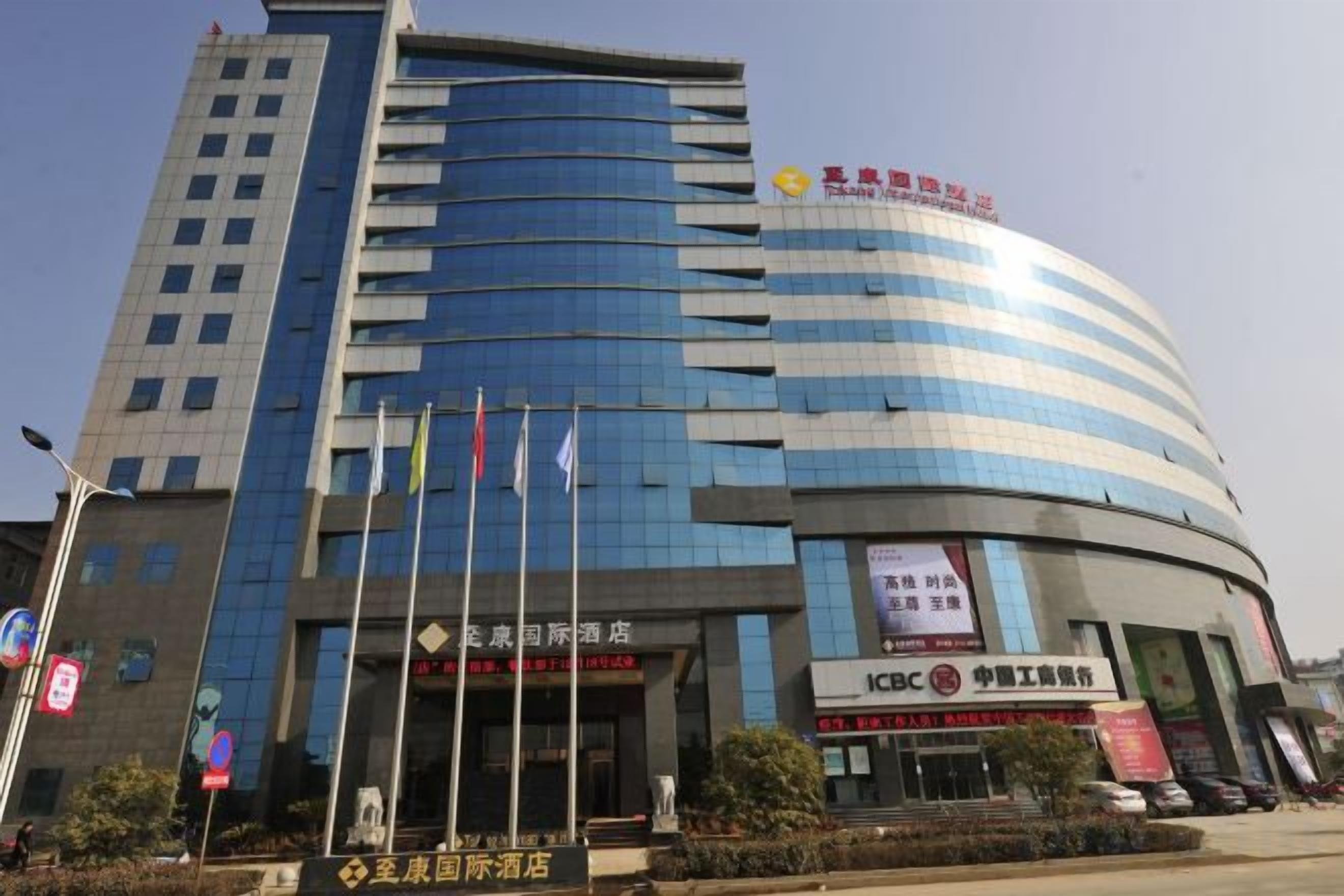 Un hotel de varios pisos con fachada curva, varias banderas y señalización que indica diversos servicios y comodidades.
