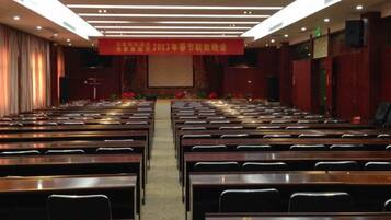 A conference room with rows of tables and chairs, a stage at the front, and a banner above.