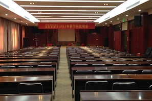 A conference room with rows of tables and chairs, a stage at the front, and a banner above. - Tokang International Hotel (Tongshan)