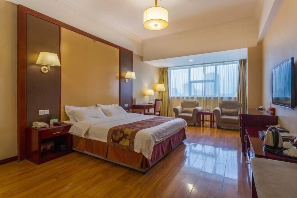 A hotel room with a bed, bedside tables, a desk, a chair, a TV, and a window with curtains.