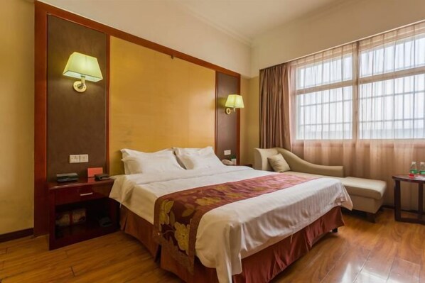 Habitación de hotel con cama, lámparas de noche, una silla, una mesita y ventana con cortinas.
