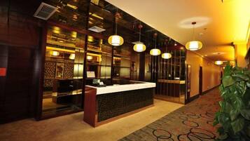 A hotel reception area with a reception desk, a plant, and a patterned carpet.