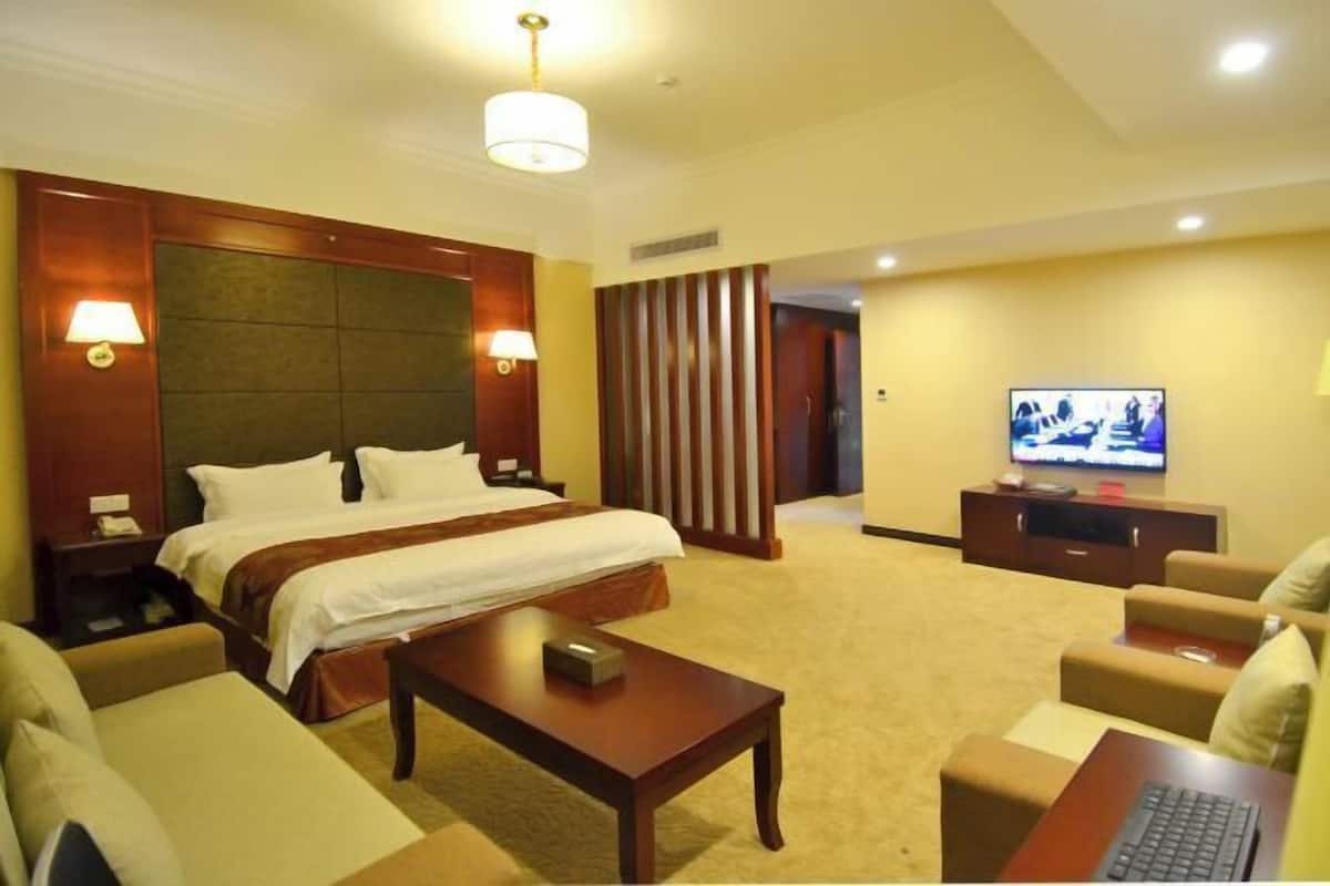 A hotel room with a large bed, a television, a desk, and a sofa.