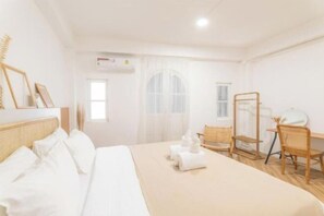 Quarto de hotel com cama, escrivaninha e cadeira. Há uma janela com cortinas, um espelho e um ar condicionado fixado na parede.