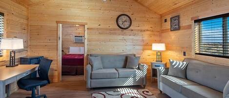 Interior acogedor de una cabaña de troncos con techo de madera, un sofá, un escritorio y un reloj en la pared.