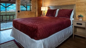 Une chambre dans une cabane en bois, avec un grand lit, une table de chevet, une lampe et une vue sur les montagnes.