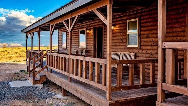 Une cabane en bois dotée d’un porche et de nombreuses fenêtres, située dans un paysage désertique.
