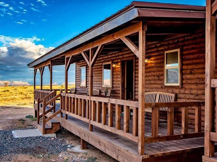 Una cabaña de madera con un porche y varias ventanas, sobre un paisaje desértico.