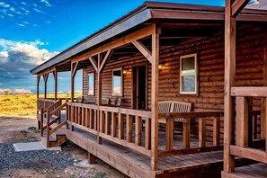 Une cabane en bois dotée d’un porche et de nombreuses fenêtres, située dans un paysage désertique.