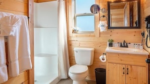 Une salle de bain rustique, aménagée dans une cabane en bois, avec des toilettes, un lavabo et une douche.