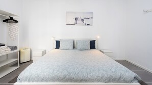 Ein schlicht eingerichtetes Schlafzimmer mit Bett, Nachttisch, Kleiderschrank und einem Wandbild.