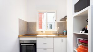 Eine kleine Küche mit Backofen, Spüle und Fenster mit geöffneten Rollläden.