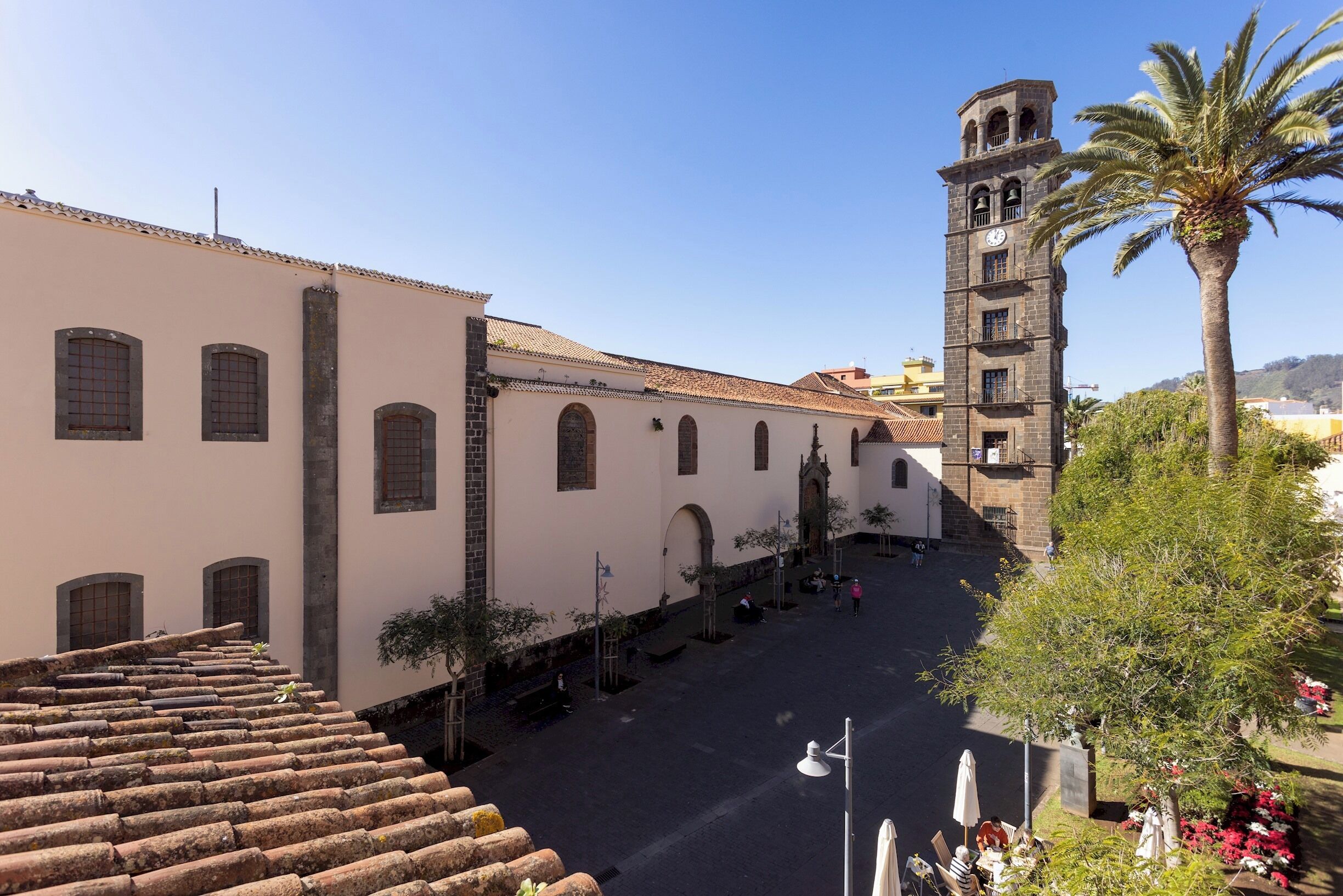 A historic building with a clock tower, a courtyard with palm trees, and a staircase leading to an upper level.