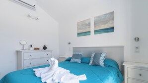 A neatly made bed with a blue bedspread and white towels, a white bedside table with a lamp, and two paintings of a seascape on the wall. - Home2Book Green Oasis Charming Duplex Maspalomas (Maspalomas)