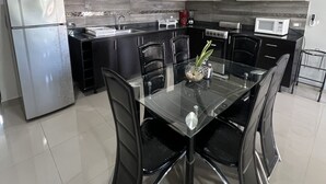 A modern kitchen with a dining area, featuring a refrigerator, stove, microwave, and black chairs around a glass table. - Villas Paraiso (Mérida)
