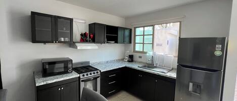Une cuisine moderne avec des meubles de couleur sombre, un réfrigérateur en acier inoxydable, un four à micro-ondes et une cuisinière à gaz.