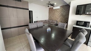 A modern dining area with a dark wooden table, grey upholstered chairs, and a patterned sofa. - Villas Paraiso (Mérida)
