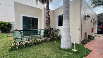 A modern building with a glass balcony, a palm tree, and a small garden area.