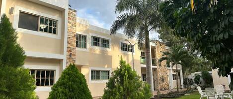 A modern multi-story building with a stone facade, multiple windows, and a well-maintained lawn with trees and outdoor furniture.