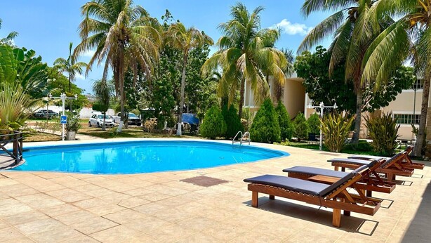 A swimming pool with lounge chairs, palm trees, and a clear blue sky. - Villas Paraiso (Mérida)