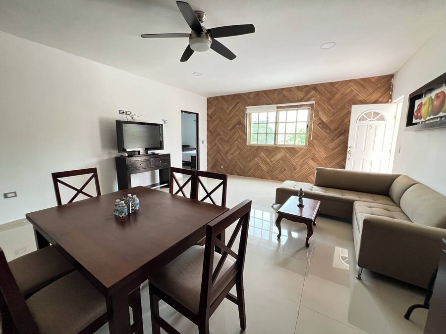 A dining area with a table and chairs, a television on a stand, a sofa, and a window with a view.