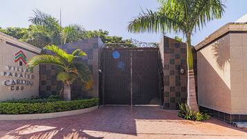 Villa Paraíso Cardin C69 entrance with a gated driveway, palm trees, and a tiled pathway.