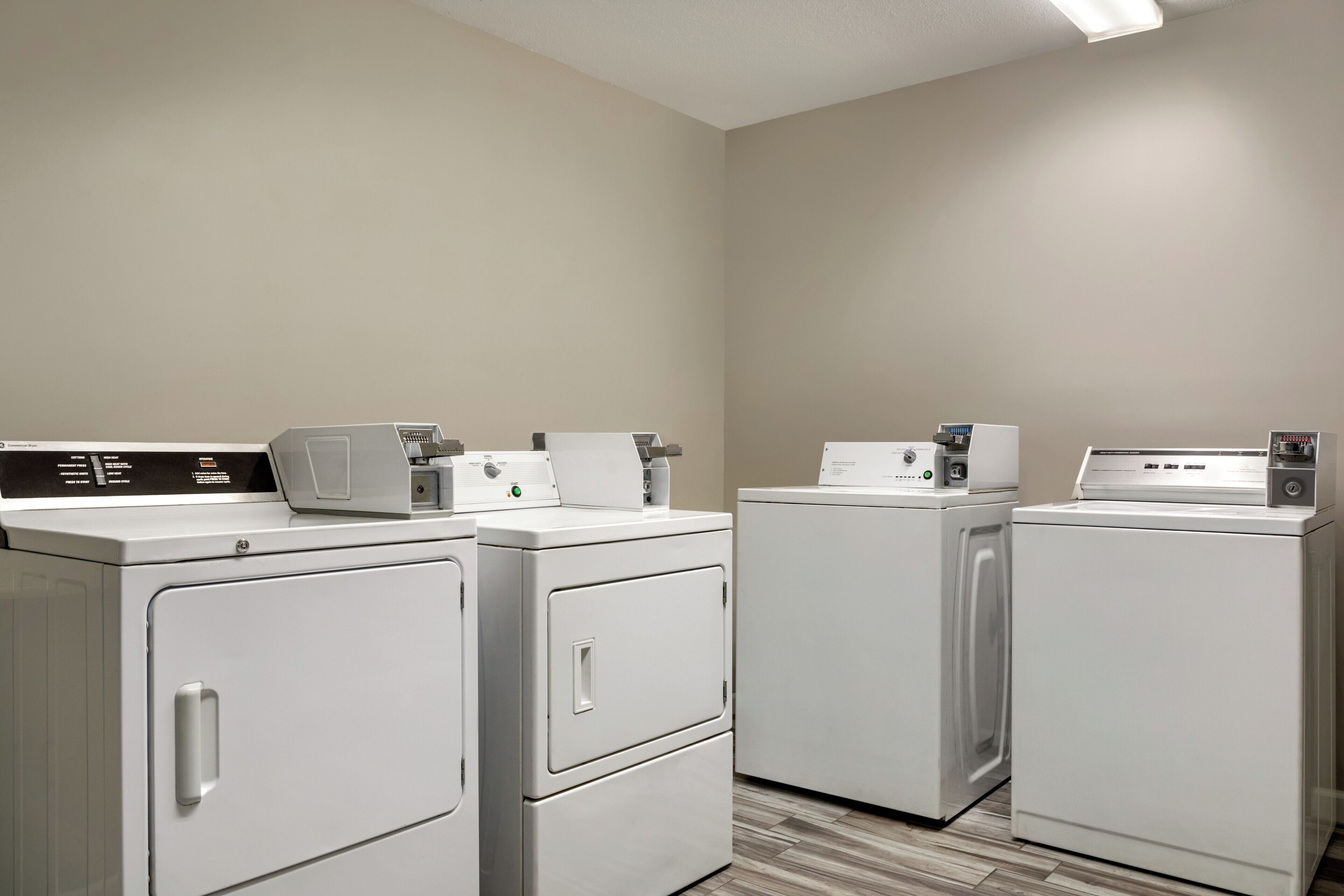 A laundry room with four white washing machines and dryers, a control panel, and a tiled floor.