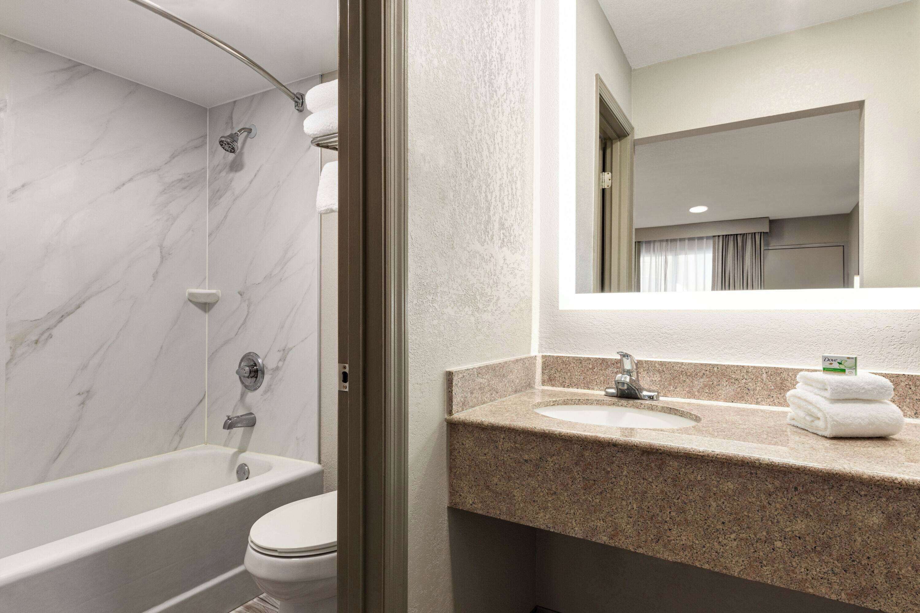 Un baño moderno con ducha de mármol, inodoro y lavamanos de granito con espejo superior.