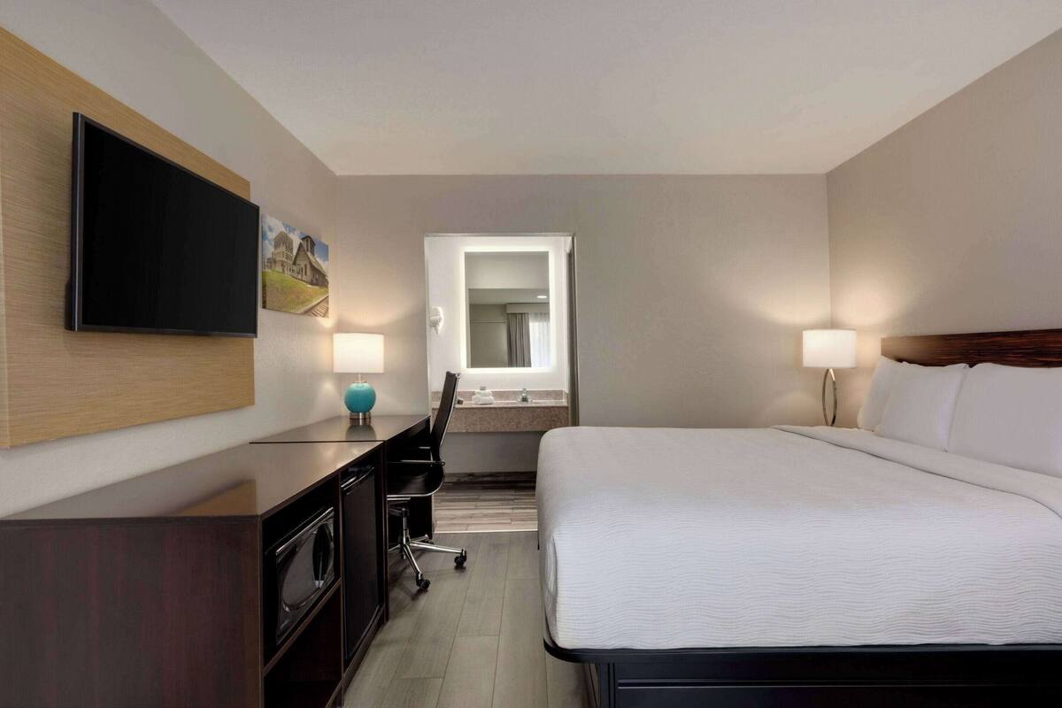 Une chambre d’hôtel comprenant un lit, un bureau avec un téléviseur à écran plat, une lampe de bureau, une chaise, un miroir et une fenêtre.