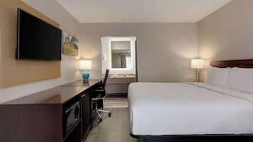 Una habitación de hotel con cama, escritorio con televisor de pantalla plana, lámpara de escritorio, silla, espejo y ventana.