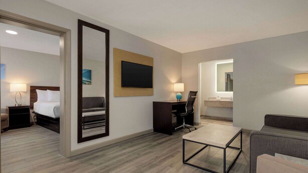 A hotel room with a bed, a desk, a chair, a sofa, a mirror, and a bathroom. - Baymont By Wyndham Emporia Va (Emporia)