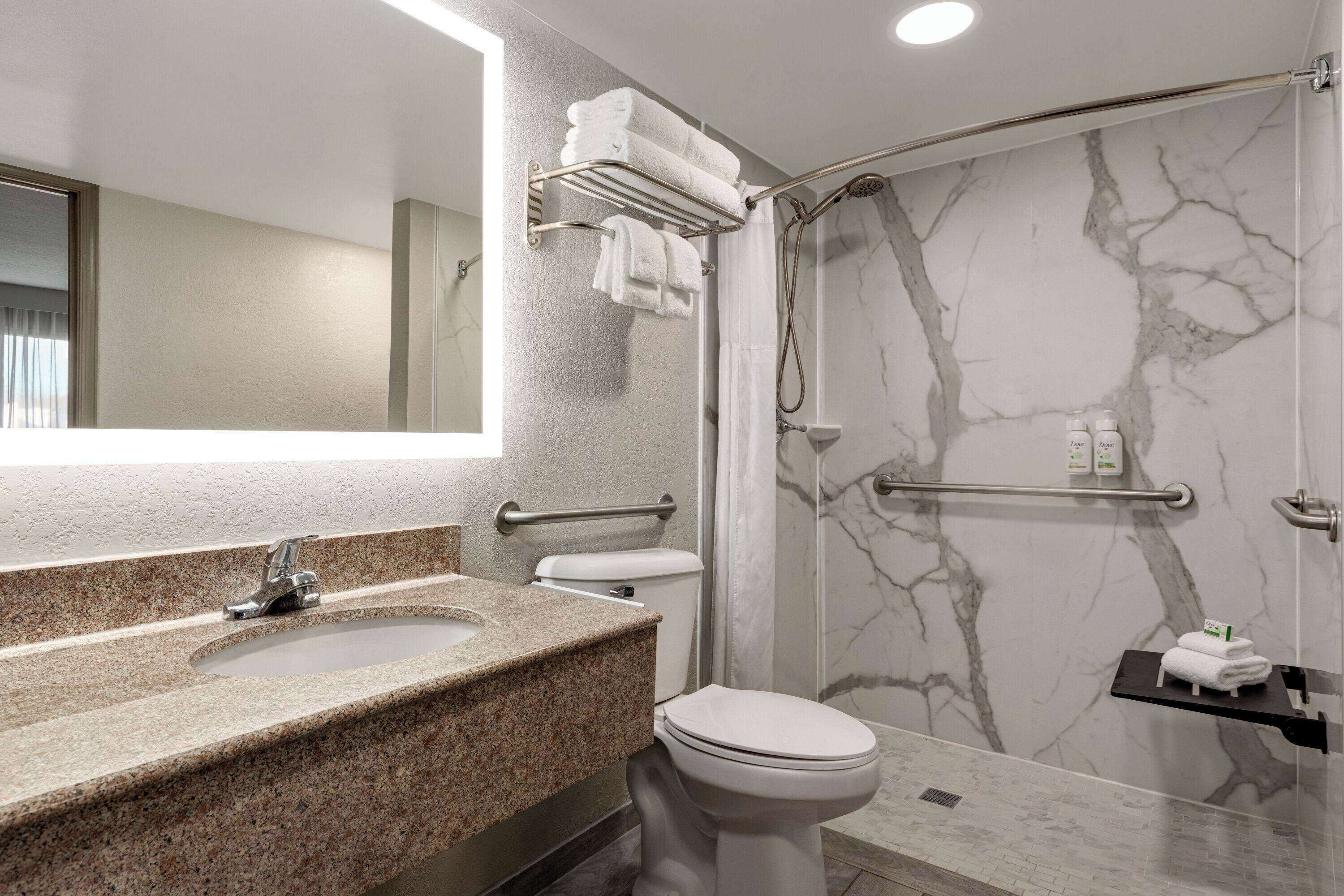A modern bathroom with a granite countertop sink, a white toilet, a glass-enclosed shower, and marble walls.