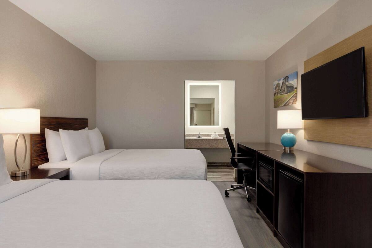 Une chambre d’hôtel avec deux lits, un bureau, une chaise, une télévision et une salle de bain visible à travers une porte ouverte.