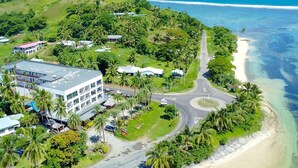 An aerial view of a coastal area with a road curving along the beach, surrounded by lush greenery and palm trees. - Ramada Suites By Wyndham Seafront Coral Coast (Korotogo)