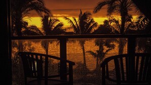 A view from a balcony with two wooden chairs, overlooking a sunset over a body of water with palm trees. - Ramada Suites By Wyndham Seafront Coral Coast (Korotogo)