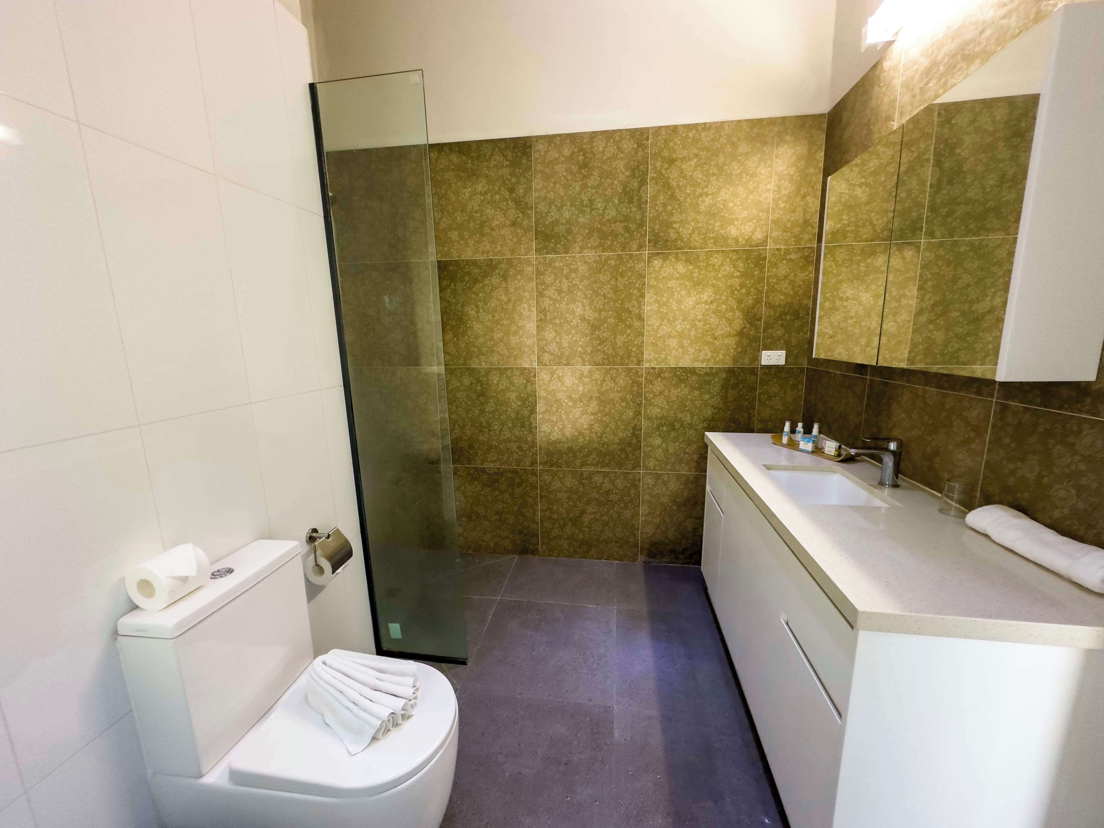 Une salle de bain moderne avec une douche à parois de verre, des toilettes blanches et un meuble-lavabo avec un évier et un miroir.