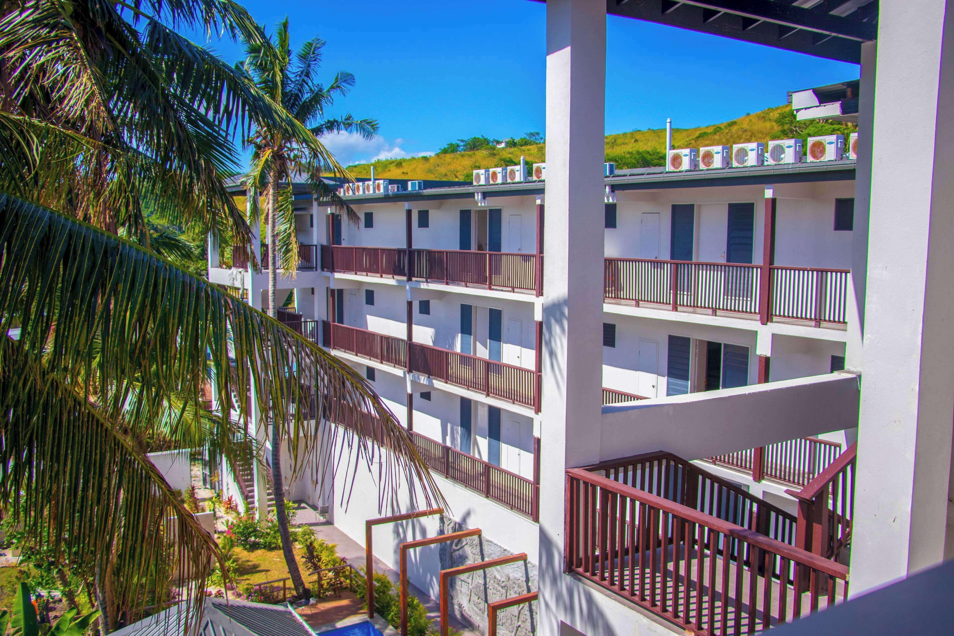 A multi-story hotel with balconies, air conditioning units, and a view of a hillside.