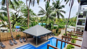 A swimming pool with lounge chairs, a covered seating area, and a view of palm trees and buildings. - Ramada Suites By Wyndham Seafront Coral Coast (Korotogo)
