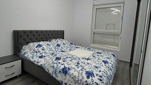 Une chambre à coucher comprenant un lit, une table de chevet, une fenêtre avec des stores et un luminaire au plafond.
